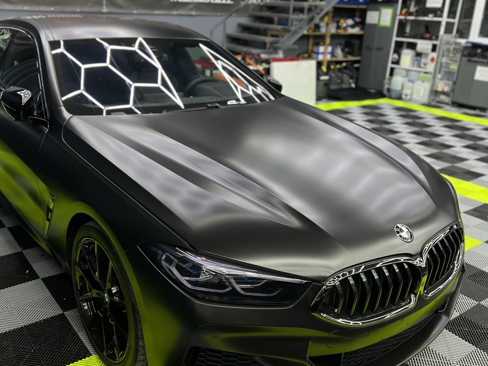 BMW coupe colantat în verde foarte închis mat, văzut din față-stânga în atelier