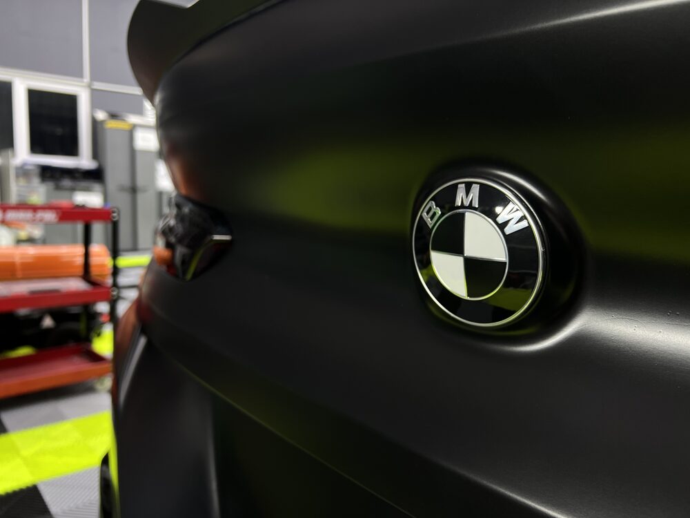 Detaliu macro al emblemei BMW pe caroseria colantată în verde mat