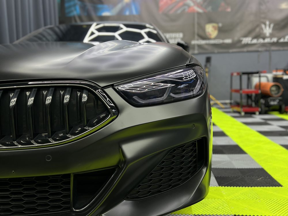 Detaliu frontal al unui BMW verde închis mat, cu grila și farul drept în prim-plan