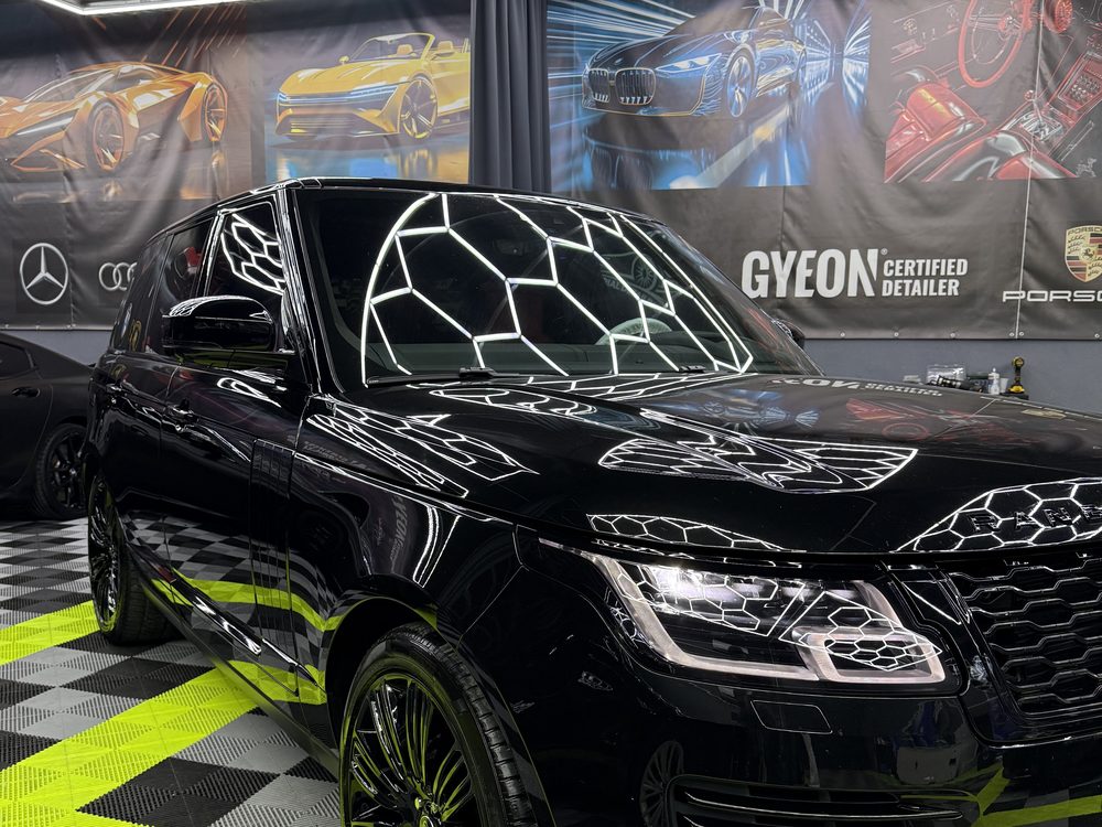Range Rover negru lucios văzut din față-stânga sub luminile atelierului