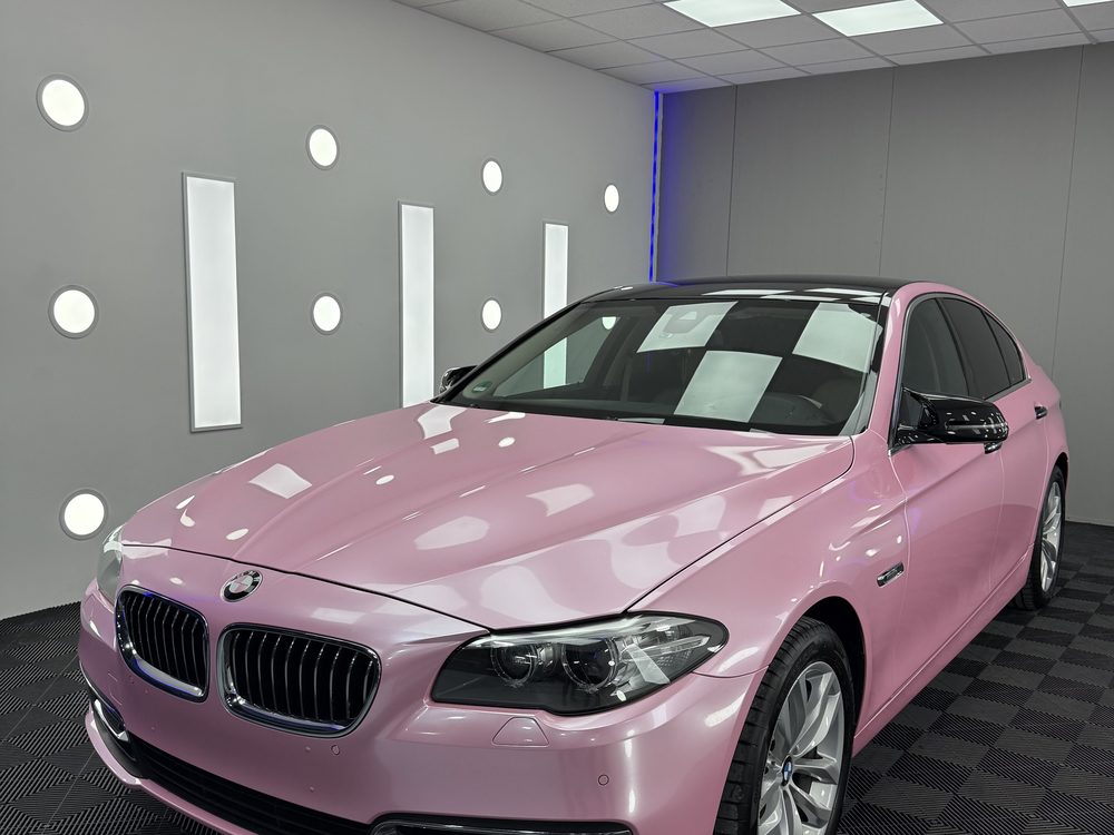 BMW sedan colantat în roz lucios, fotografiat din față-stânga într-un spațiu de detailing