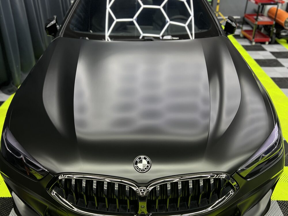 BMW coupe colantat în verde foarte închis mat, văzut din față, cu capota și grila în prim-plan