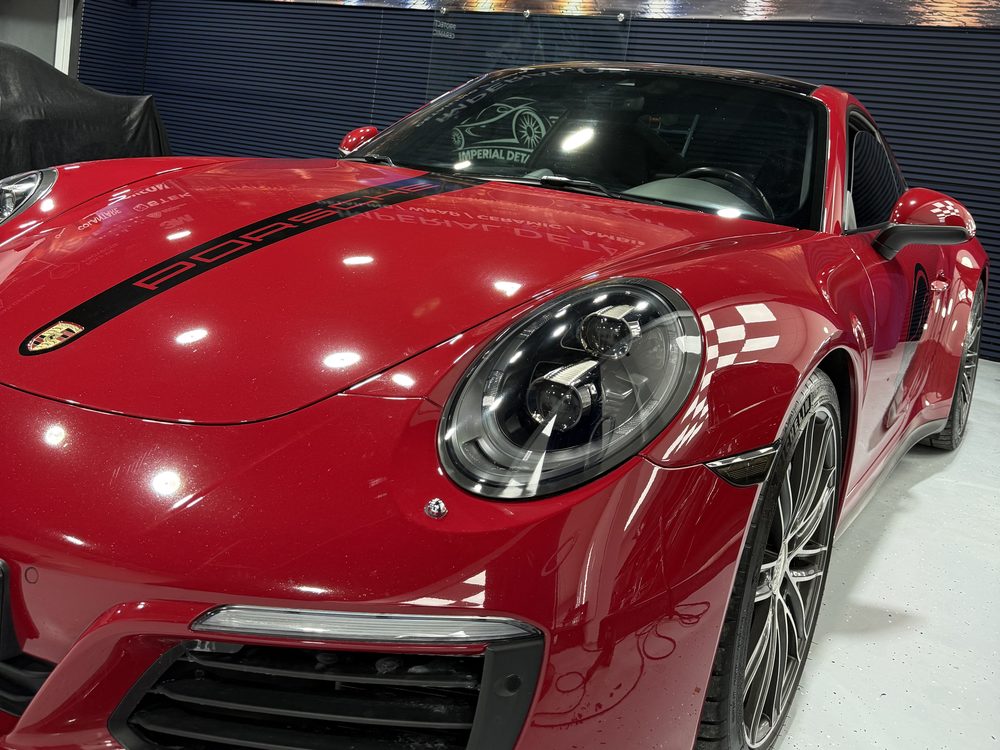 Porsche 911 roșu văzut din față-stânga, cu dungă neagră pe capotă și decor în carouri pe aripă, în atelierul Imperial Detailing Oradea