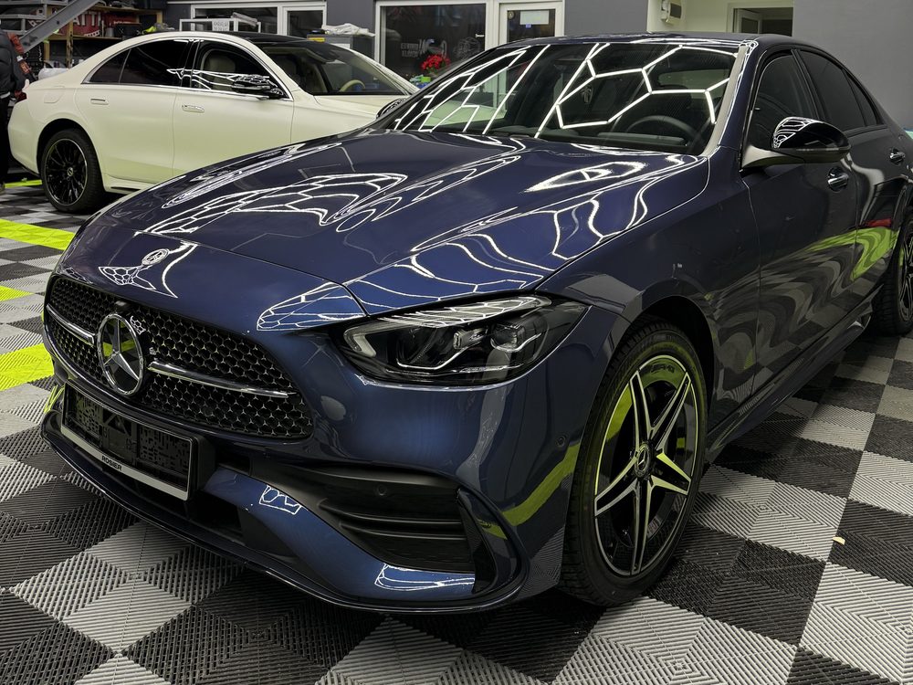 Mercedes-Benz albastru închis văzut din față-stânga, cu luminile hexagonale ale atelierului oglindite în capotă