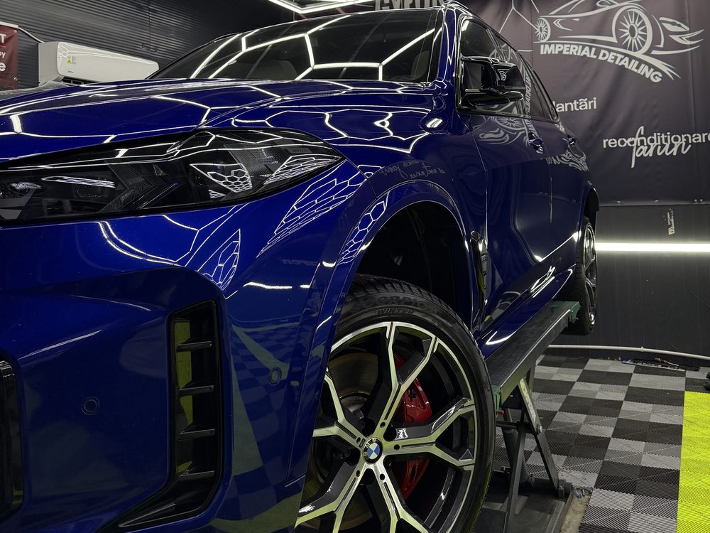 SUV BMW albastru intens, cadru apropiat din față-stânga, cu etrier roșu și emblema M pe capacul jantei, ridicat pe suport în atelier