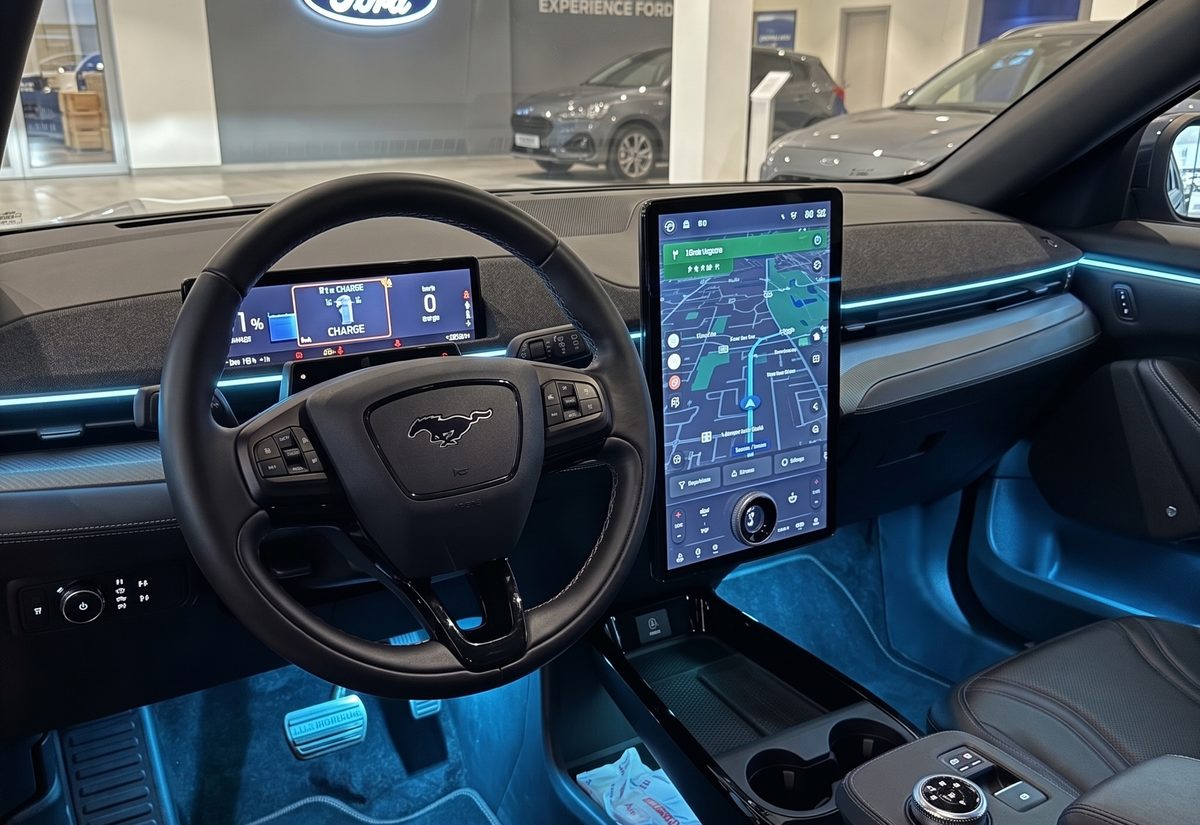 Interior Ford Mustang Mach-E într-un showroom auto, cu banda de lumină ambientală albastră pe bord și iluminare albastră în zona picioarelor